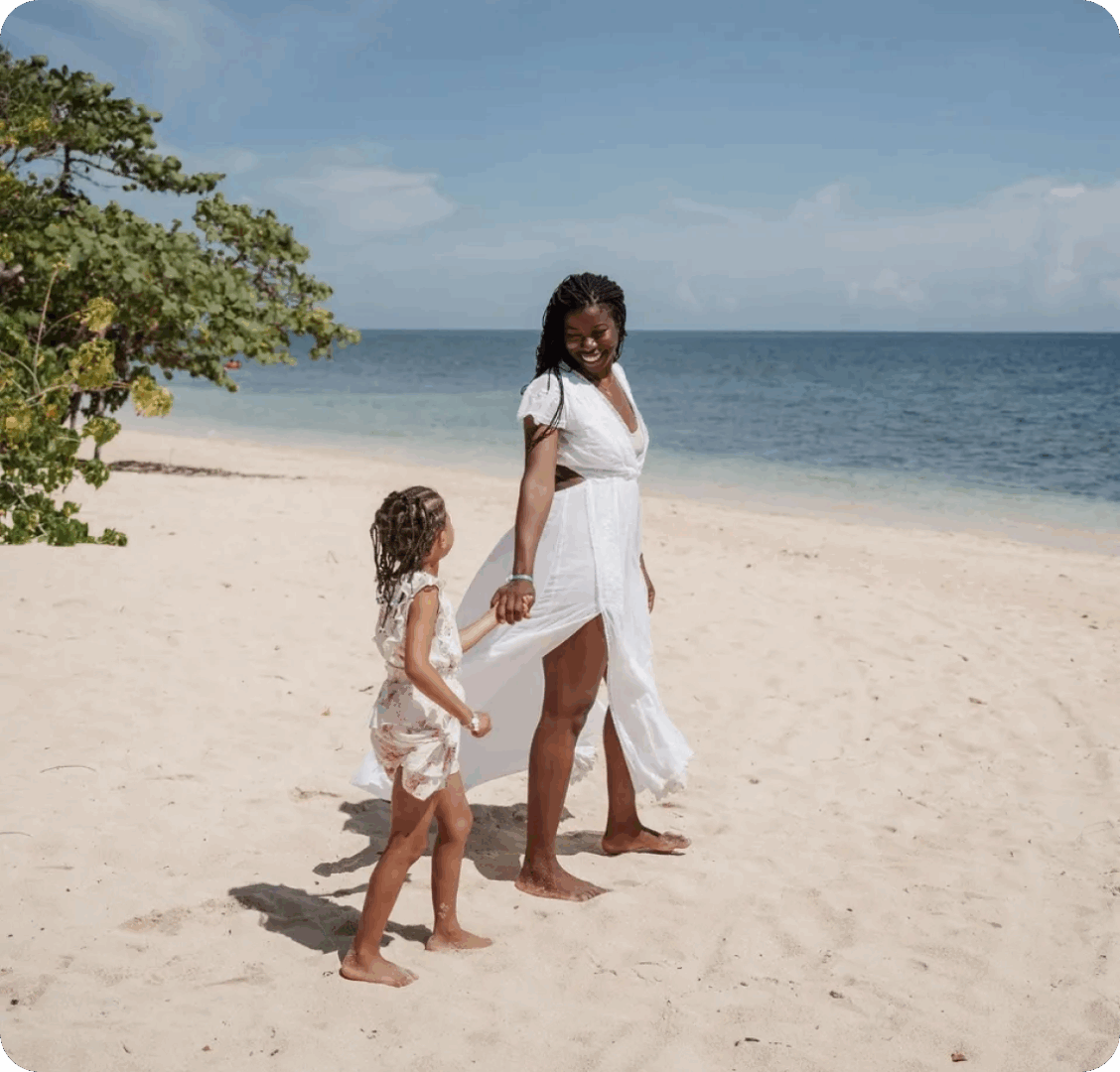 Mother and daughter walking on sandy beach.