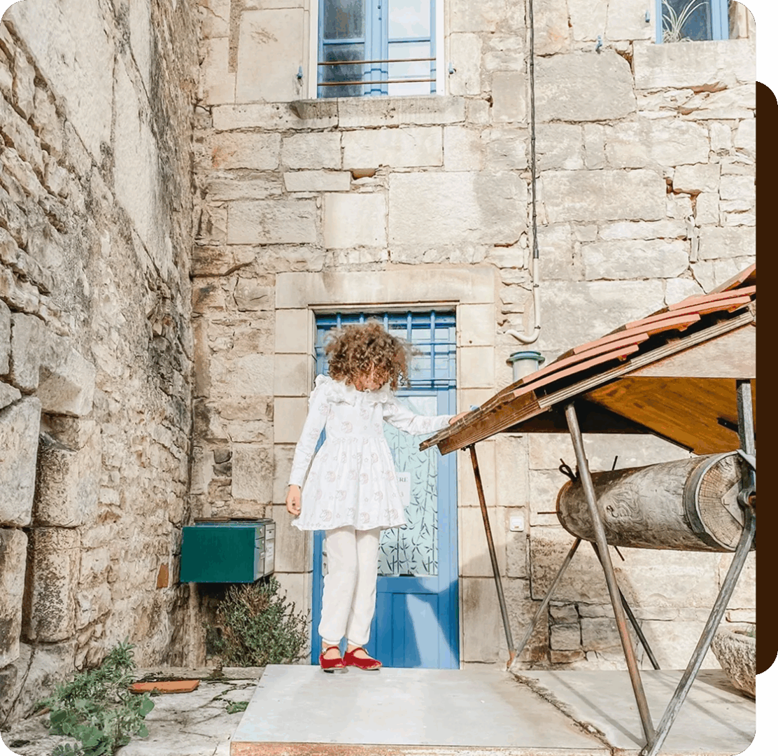 Child in white dress near stone building.