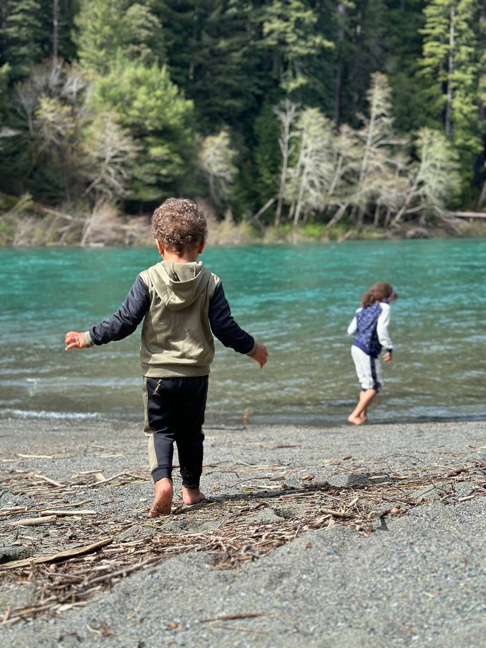Two children walking barefoot along the turquoise Smith River at Jedediah Smith Redwoods
