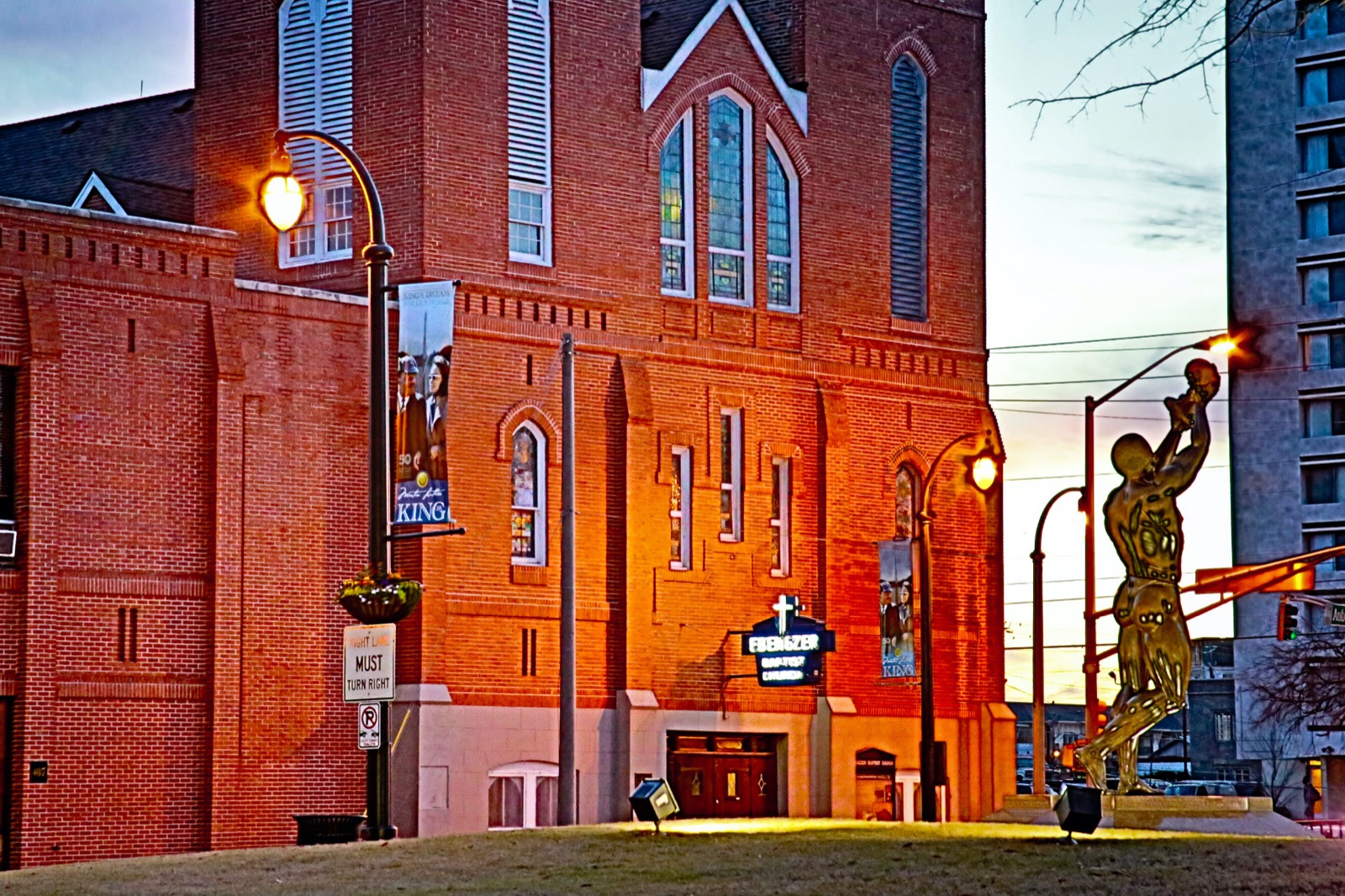 Ebenezer Baptist Church in Atlanta bathed in golden sunset light, with the Behold sculpture reaching skyward beside the historic red brick facade