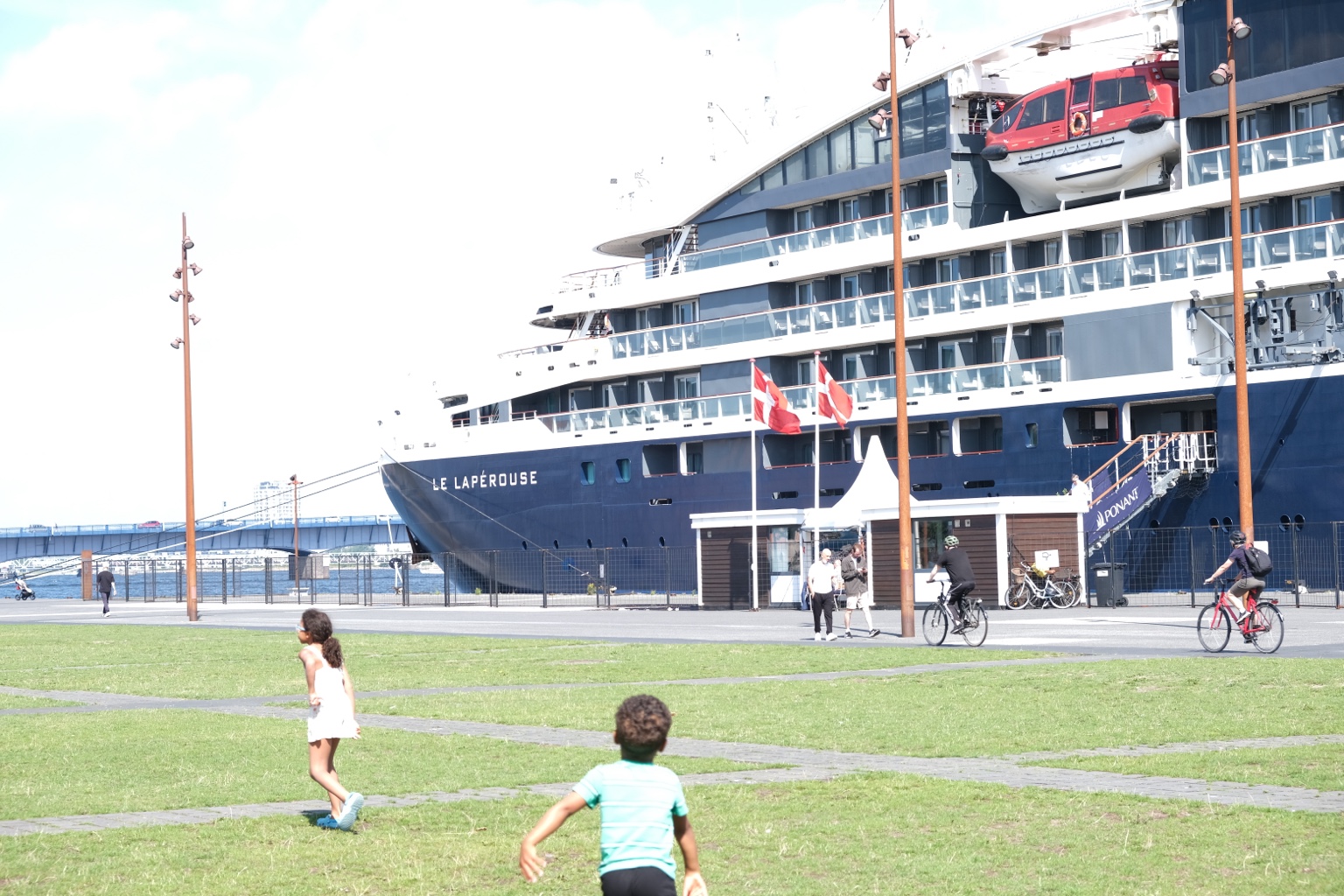 Children playing on a waterfront lawn beside a docked ship