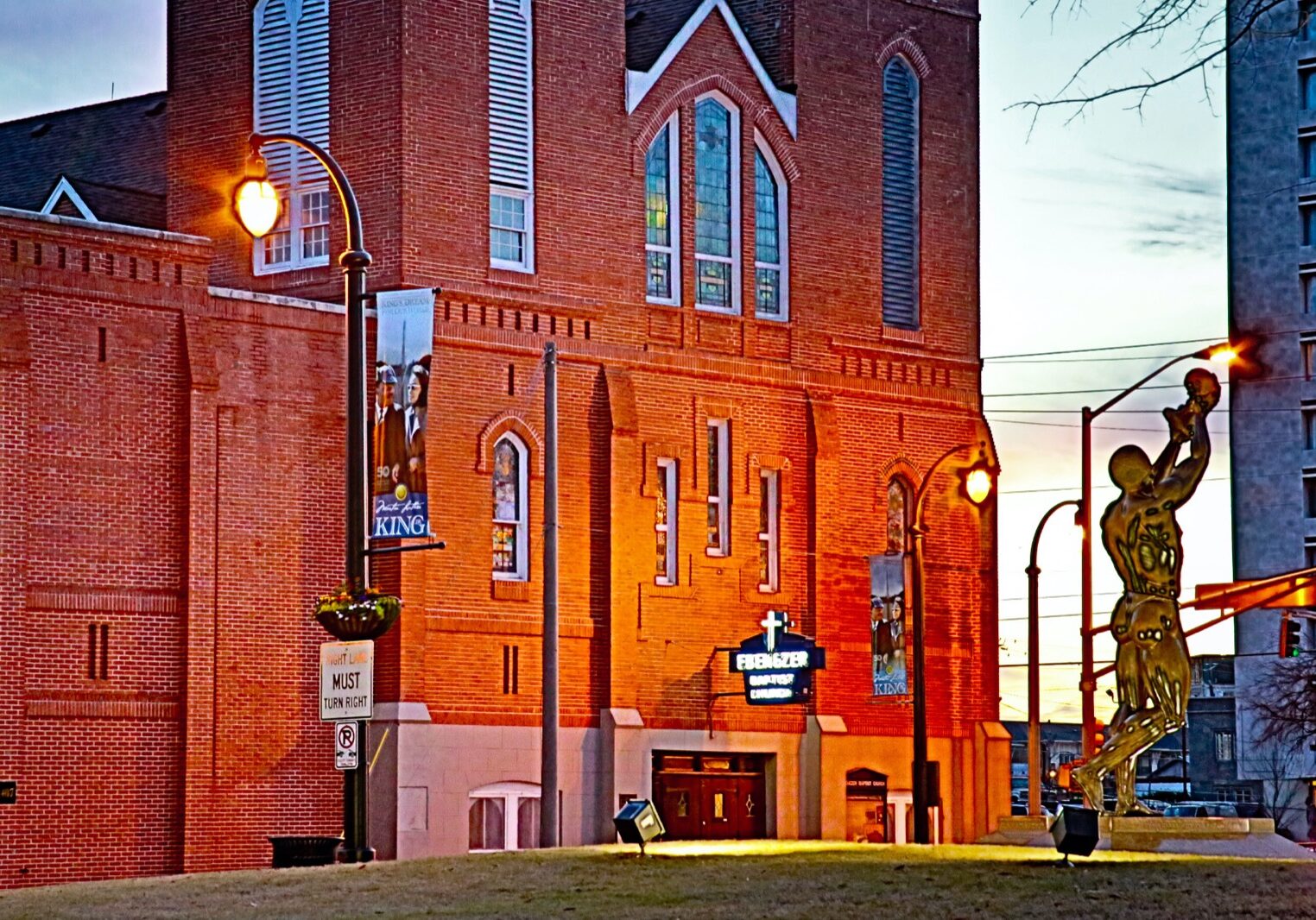 Ebenezer Baptist Church in Atlanta bathed in golden sunset light, with the Behold sculpture reaching skyward beside the historic red brick facade