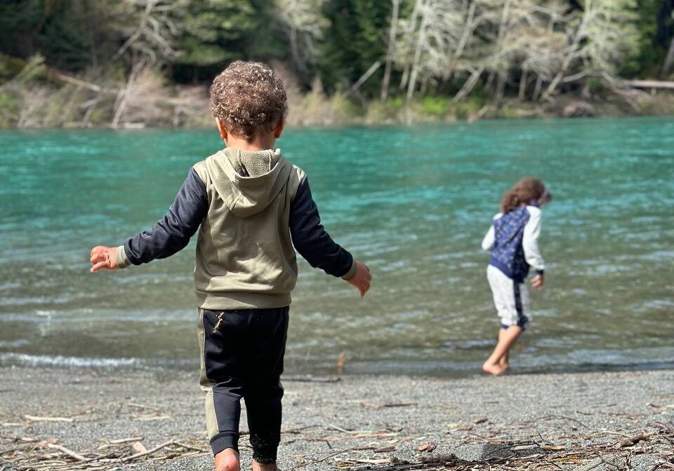 Two children walking barefoot along the turquoise Smith River at Jedediah Smith Redwoods