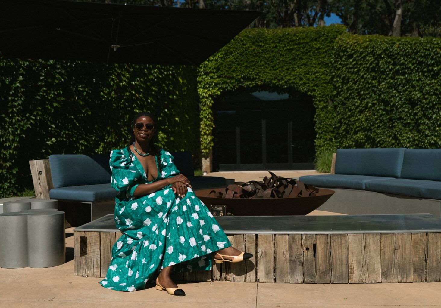 Sheba Sawyer seated on a garden terrace in a green floral dress